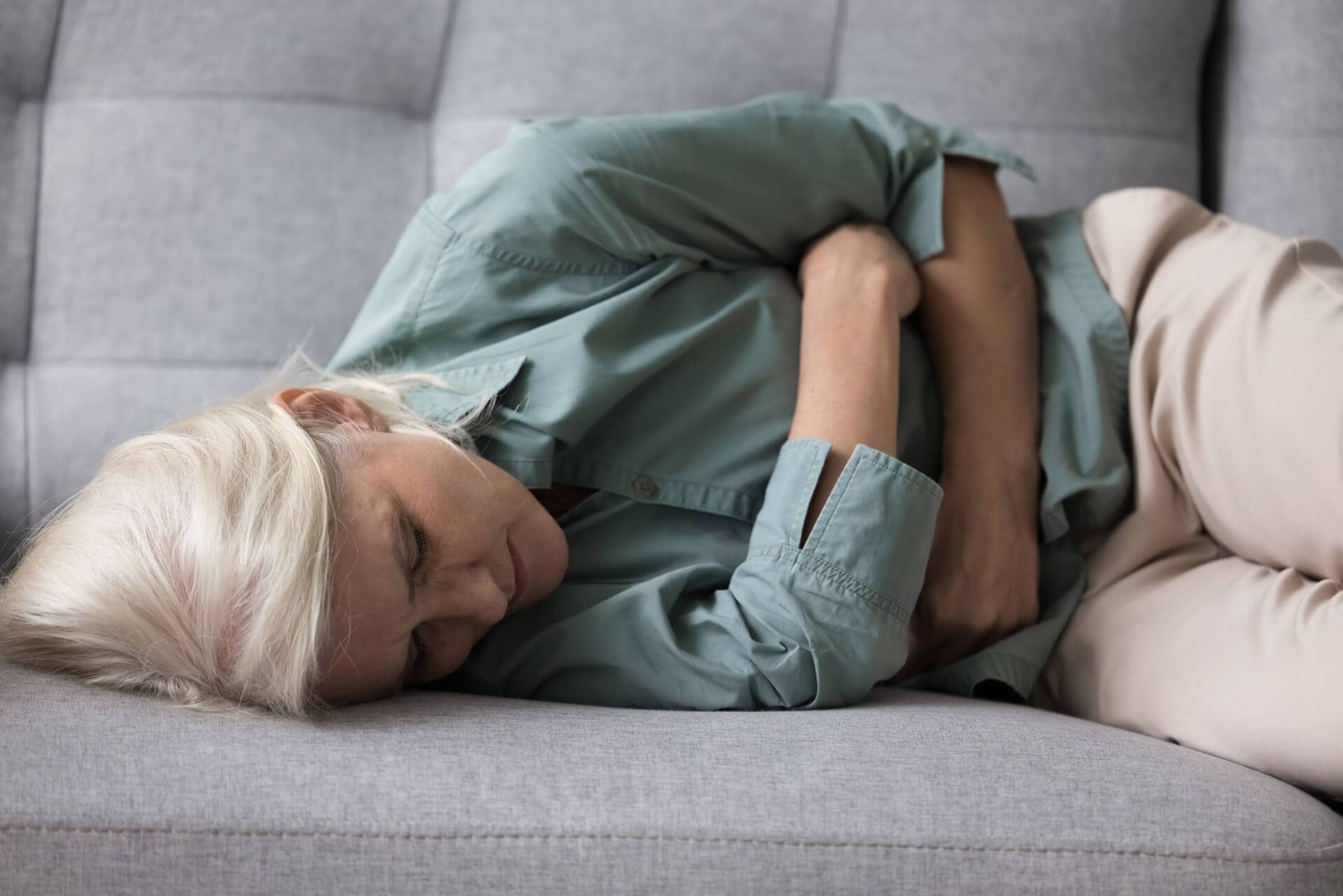 Elderly woman lying down while experiencing stomach discomfort